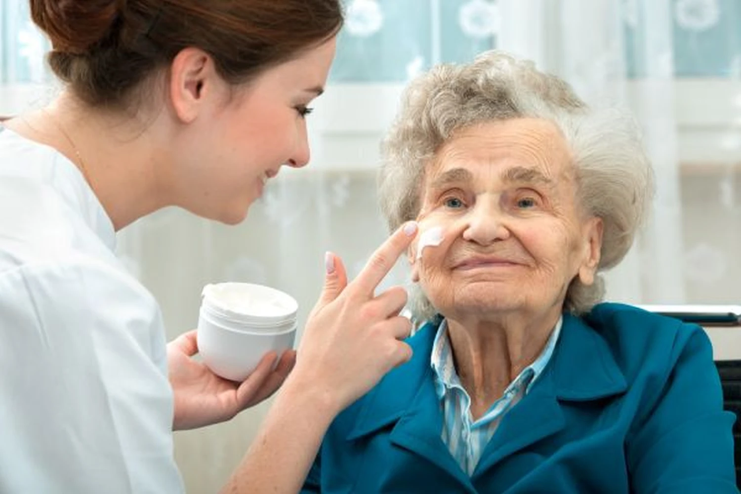 Betreuungsdienst Jaqueline - Eine Krankenschwester cremt das Gesicht einer alten Dame ein